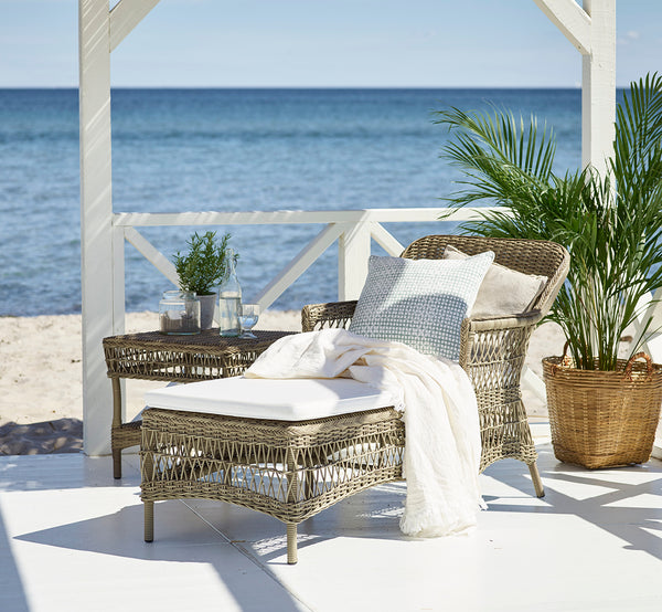 Dies ist ein Lifestyle-Bild von Olivia Exterior Sunbed i antique grey artfibre aluminium. Auf einer Steinterrasse umgeben von Garten.
