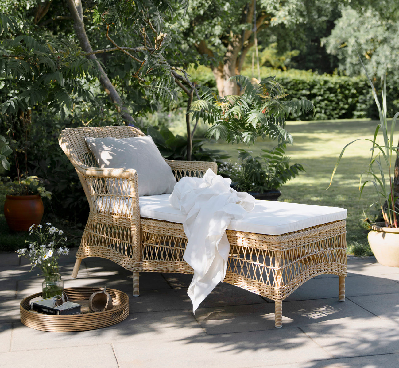 Dies ist ein Lifestyle-Bild von Olivia Exterior Sunbed i natural artfibre aluminium. In einem Garten-Setting mit weißer Decke und Kissen.