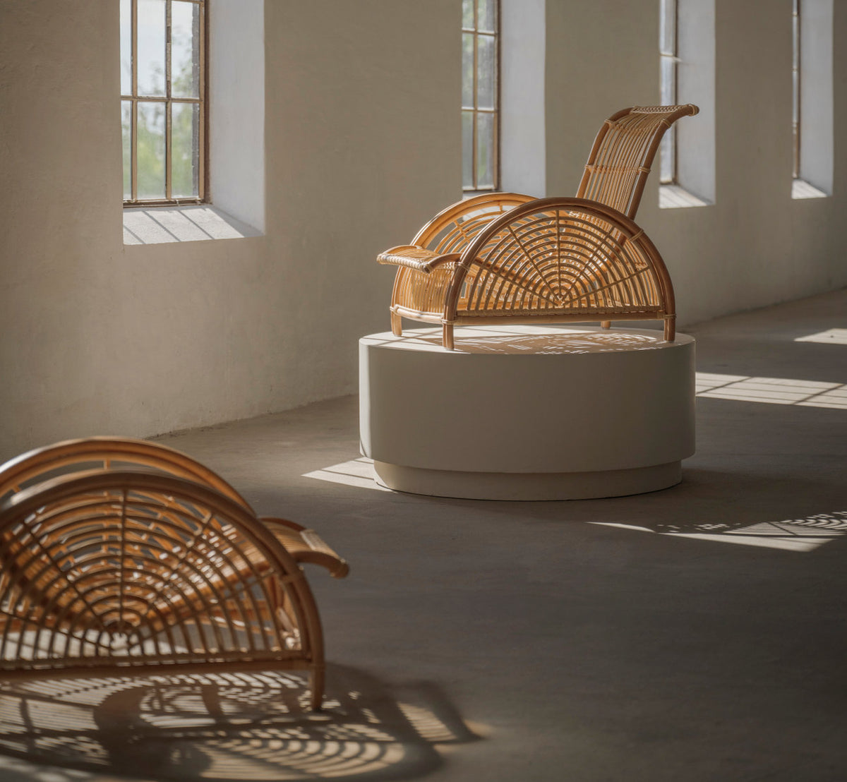 Dies ist ein Lifestyle-Bild von Paris Lounge-Sessel in polished natural rattan. Paar in einer sonnigen Galerie, einer auf einem weißen Sockel.