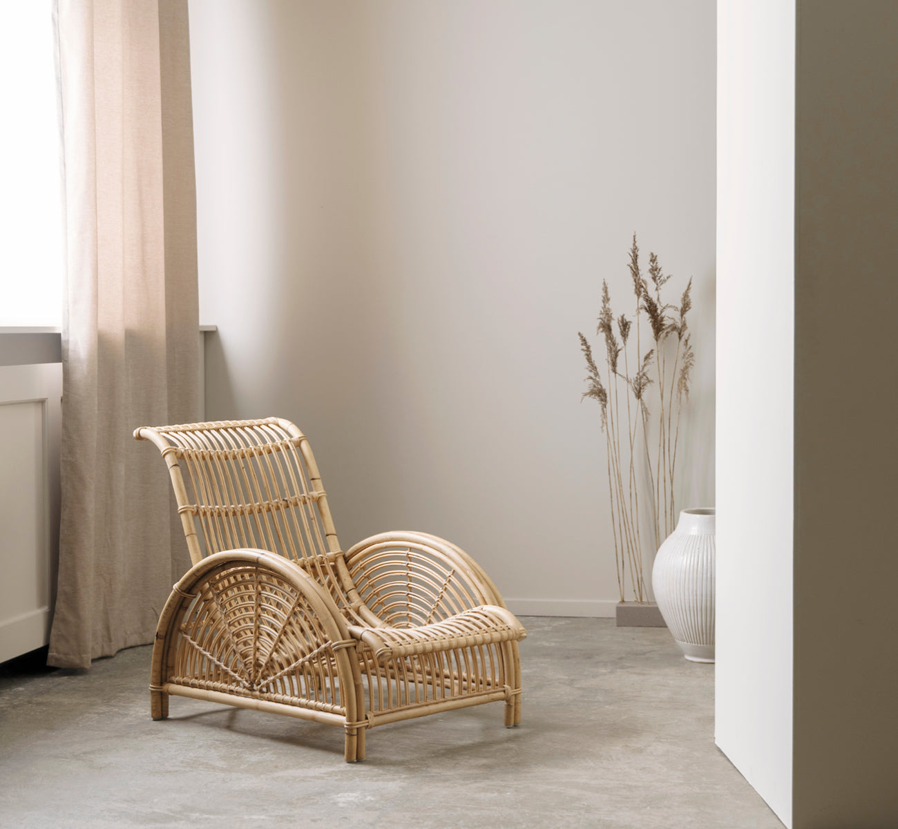 Dies ist ein Lifestyle-Bild von Paris Lounge-Sessel in polished natural rattan. Auf einem Fischgrätparkettboden neben einer passenden Bank platziert.
