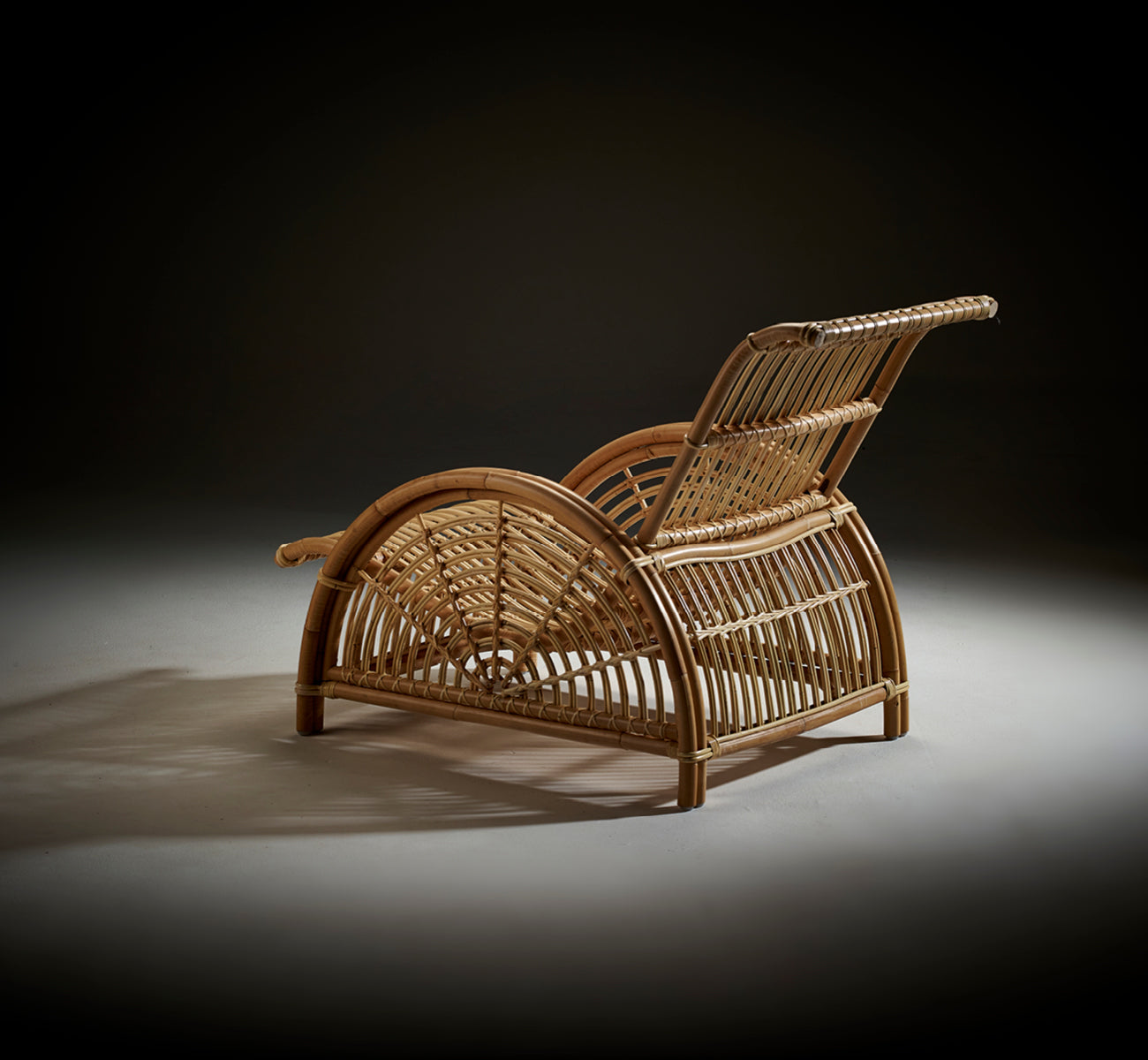 Dies ist ein Lifestyle-Bild von Paris Lounge-Sessel in polished natural rattan. Auf einem Fischgrätparkettboden neben einer passenden Bank platziert.
