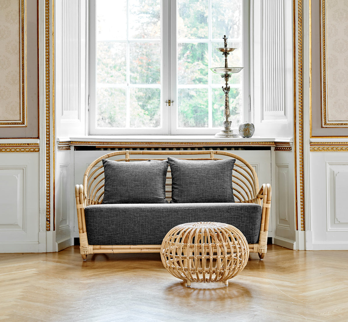 Dies ist ein Lifestyle-Bild von Charlottenborg Sofa in polished Natural Rattan, in einem eleganten klassischen Interieur mit aufwändigen goldenen.