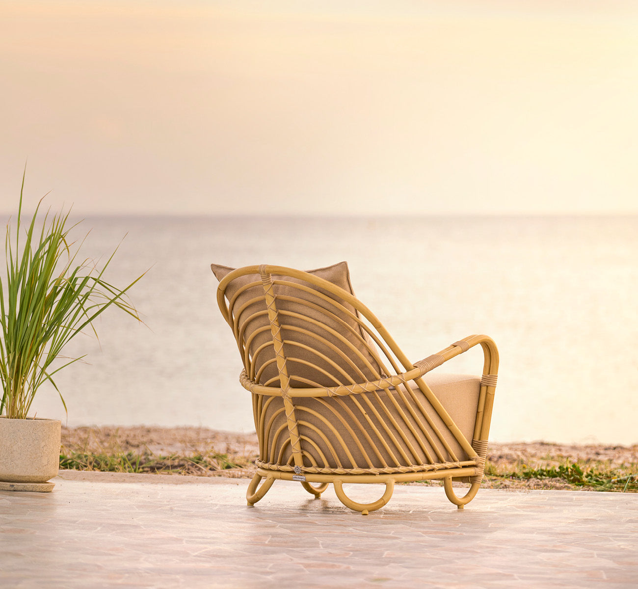 Dies ist ein Lifestyle-Bild von Charlottenborg Außen-Lounge-Sessel in natural Aluminium ArtFibre, auf einer Holzterrasse im Freien mit Blumen und.