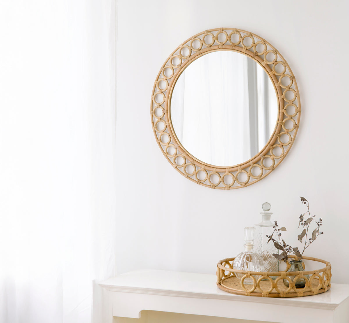 Dies ist ein Lifestyle-Bild von Mira Tray i natural rattan. Zusammen mit Mira Spiegel auf einer weißen Konsole mit Glaskaraffen präsentiert.