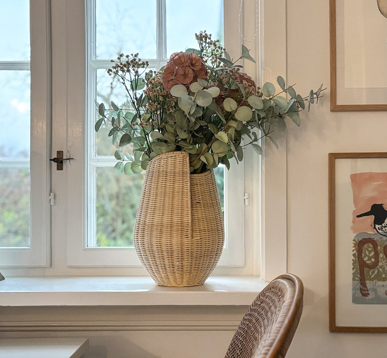 Dies ist ein Lifestyle-Bild von Aura Korb in natural core weave Iron frame, in einem hell-weißen Interieur mit Wandvertäfelung, dekoriert mit.
