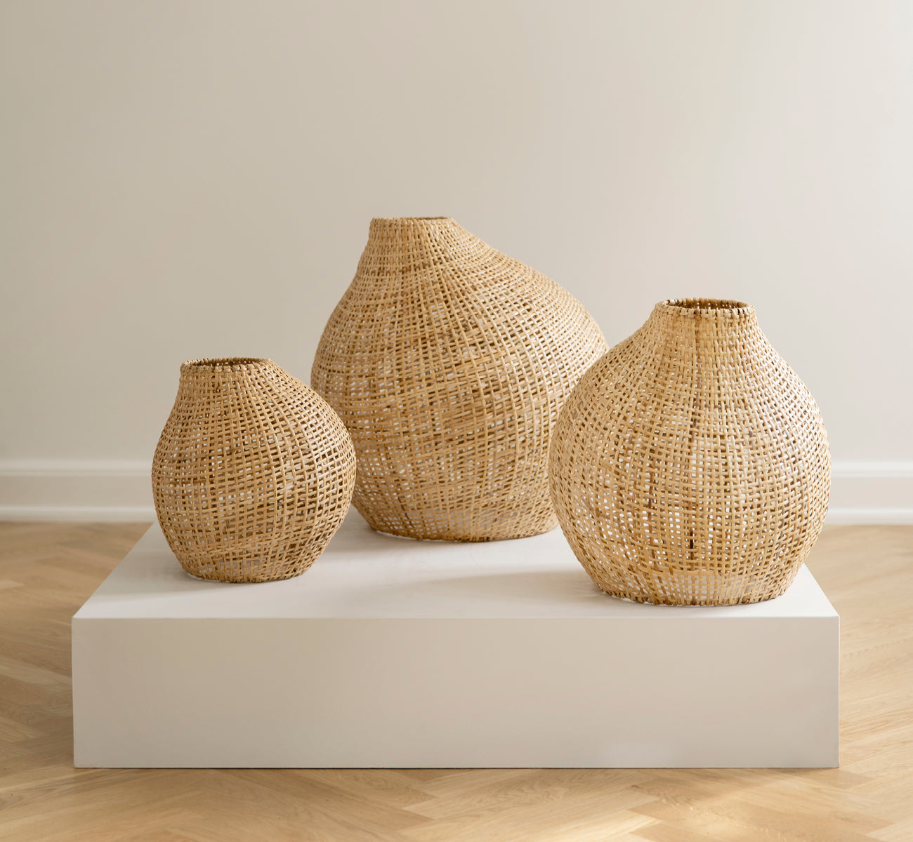 Dies ist ein Lifestyle-Bild von Figura Stehlampen-Schirm in light natural weave rattan, auf einer weißen Plattform vor einem neutralen.
