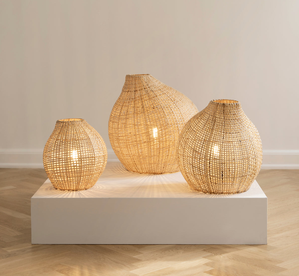 Dies ist ein Lifestyle-Bild von Figura Stehlampen-Schirm in light natural weave rattan, auf einer weißen Plattform vor einem neutralen.