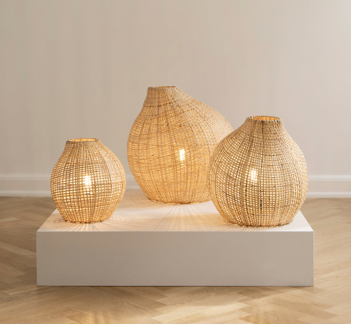 Dies ist ein Lifestyle-Bild von Figura Stehlampen-Schirm in light natural weave rattan, auf einer weißen Plattform vor einem neutralen.
