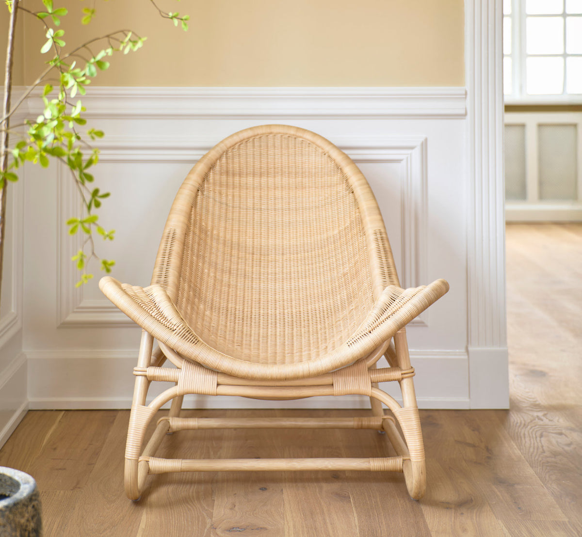 Dies ist ein Lifestyle-Bild von Pacifique Lounge-Sessel in natural core weave rattan frame. Frontansicht vor weiß vertäfelten Wänden.