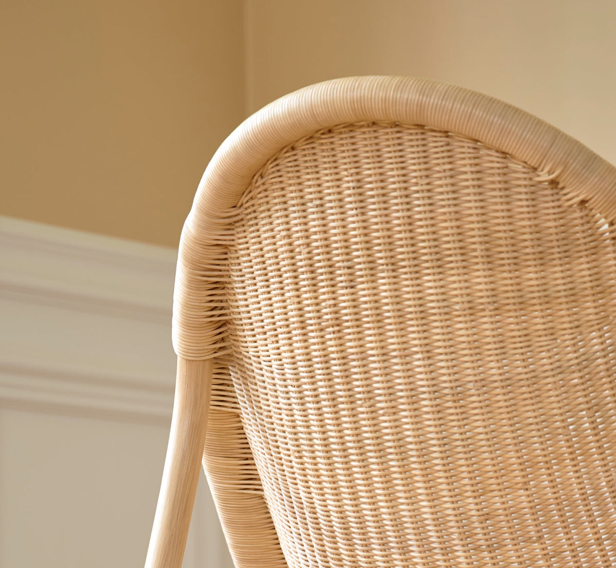 Dies ist ein Lifestyle-Bild von Pacifique Lounge-Sessel in natural core weave rattan frame. Geflochtene Lehne im weichen Licht vor einer vertäfelten Wand.