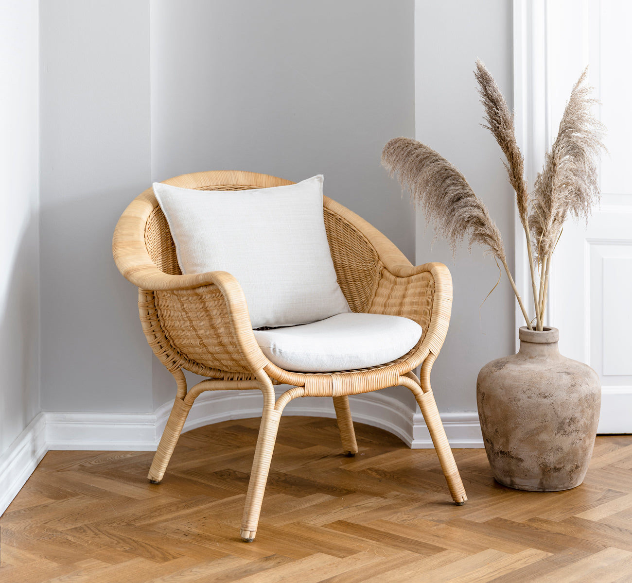 Dies ist ein Lifestyle-Bild von Madame Lounge-Sessel in natural core weave rattan frame. Gemütliche Ecke mit Fischgrätboden und Pampasgras-Vase.