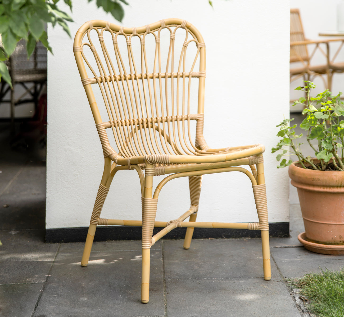 Dies ist ein Lifestyle-Bild von Margret Außen-Esszimmerstuhl in natural aluminium artfibre. Weißer Innenhof mit Terrakottatöpfen und Pflanzen.
