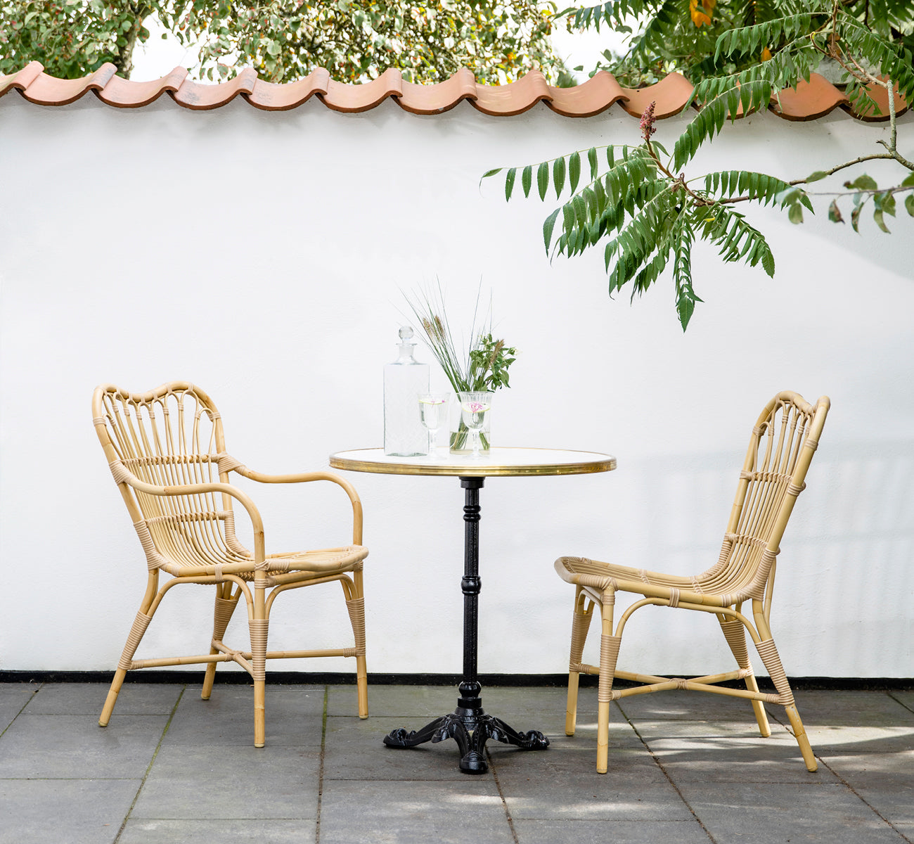 Dies ist ein Lifestyle-Bild von Margret Außen-Esszimmer-Armlehnstuhl in natural aluminium artfibre. Innenhof mit Cafétisch unter Ziegeldachüberstand.
