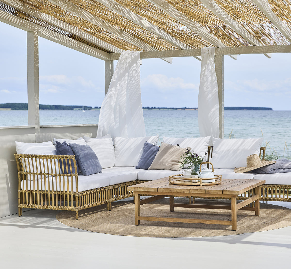 Dies ist ein Lifestyle-Bild von Maggie Sofa Eckmodul in antique aluminium artfibre. Strandpavillon mit Sofaset und Meerblick.