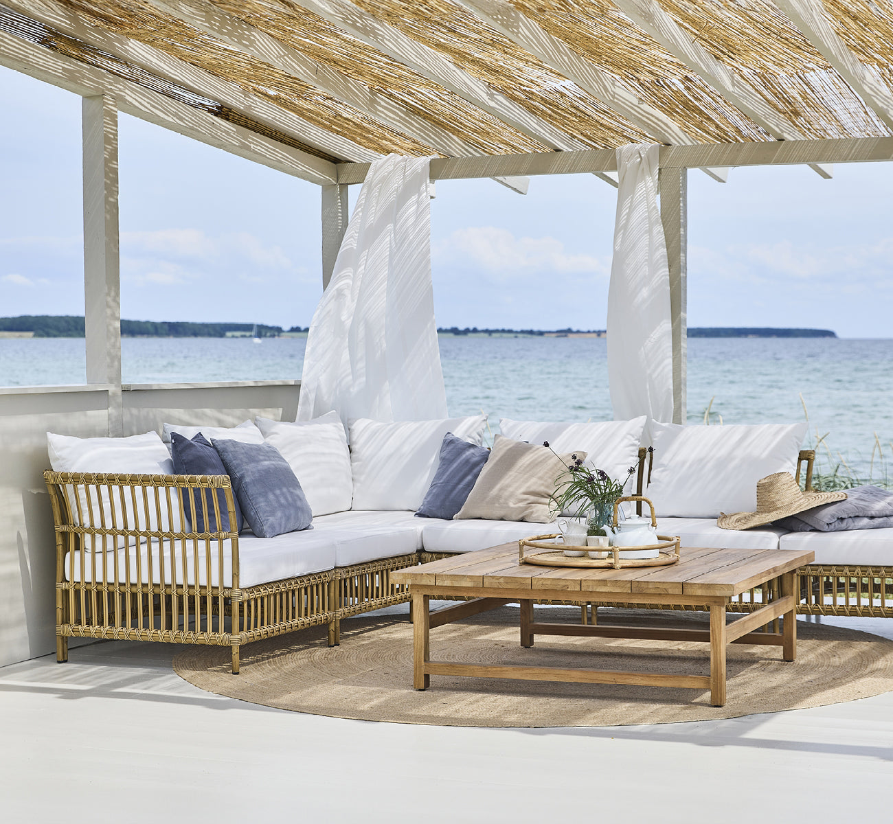 Dies ist ein Lifestyle-Bild von Maggie Sofa Eckmodul in antique aluminium artfibre. Strandpavillon mit Sofaset und Meerblick.
