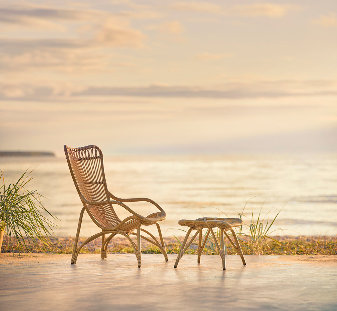 Dies ist ein Lifestyle-Bild von Monet Exterior Footstool i antique aluminium artfibre. Mit Lounge-Sessel auf einem Strandpavillon-Deck.