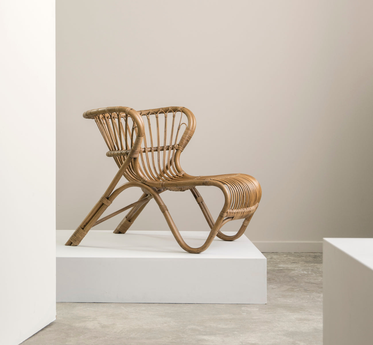 Dies ist ein Lifestyle-Bild von Fox Lounge-Sessel in polished Antique Rattan, in einem warmen Interieur mit ockerfarbener Wandvertäfelung und dunklem.