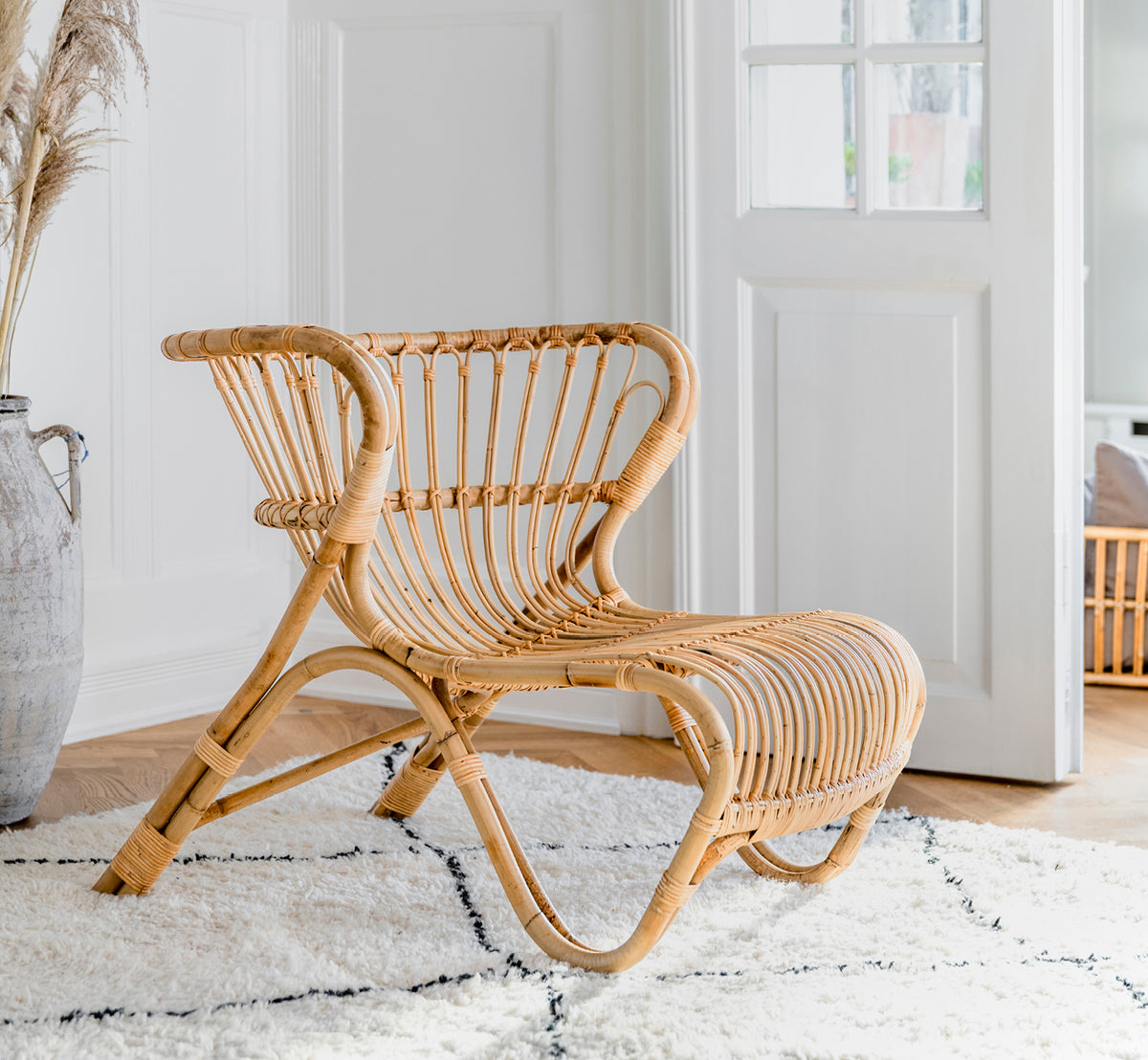 Dies ist ein Lifestyle-Bild von Fox Lounge-Sessel in polished Natural Rattan, in einem warmen Interieur mit ockerfarbener Wandvertäfelung und dunklem.