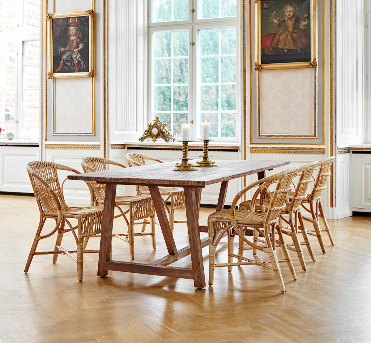 Dies ist ein Lifestyle-Bild von Robert Esszimmerstuhl in polished antique rattan. Neben einer hohen Terrakotta-Urne auf einem Fischgrätparkettboden platziert.