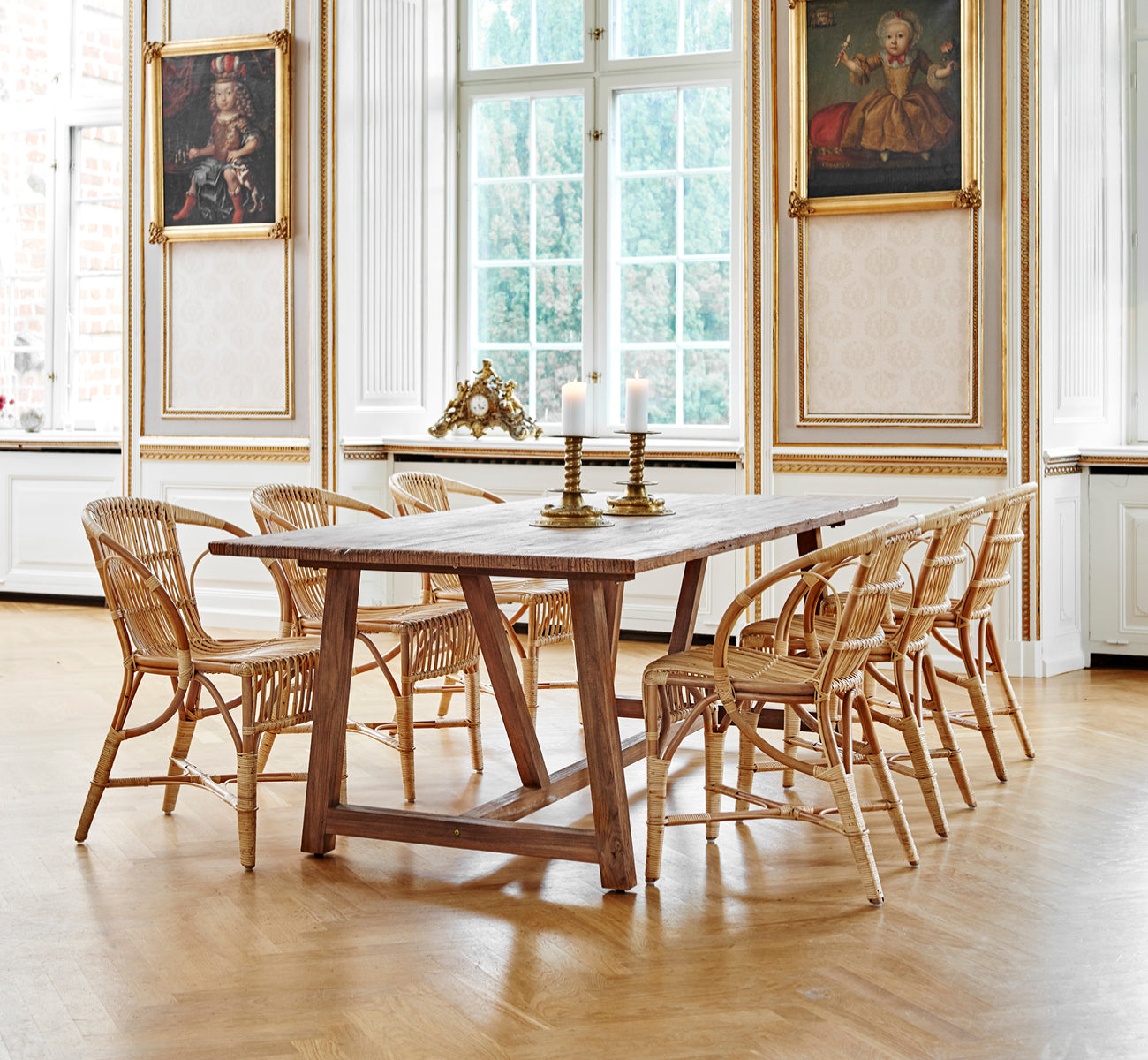 Dies ist ein Lifestyle-Bild von Robert Esszimmerstuhl in polished antique rattan. Neben einer hohen Terrakotta-Urne auf einem Fischgrätparkettboden platziert.