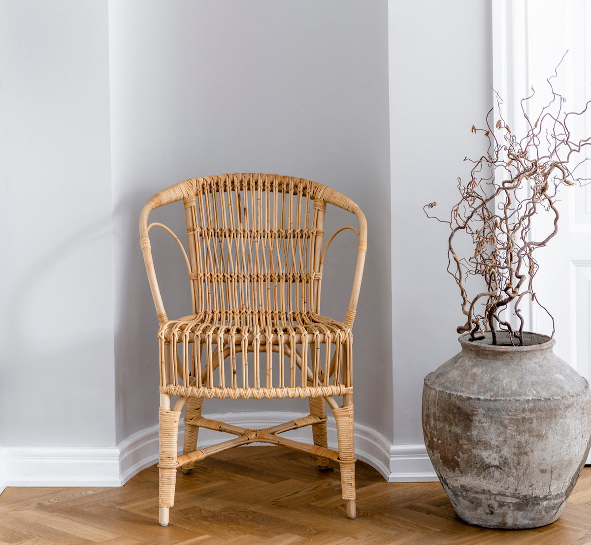 Dies ist ein Lifestyle-Bild von Robert Esszimmerstuhl in polished natural rattan. Neben einem Säulentisch mit Tulpen auf einem Juteteppich platziert.