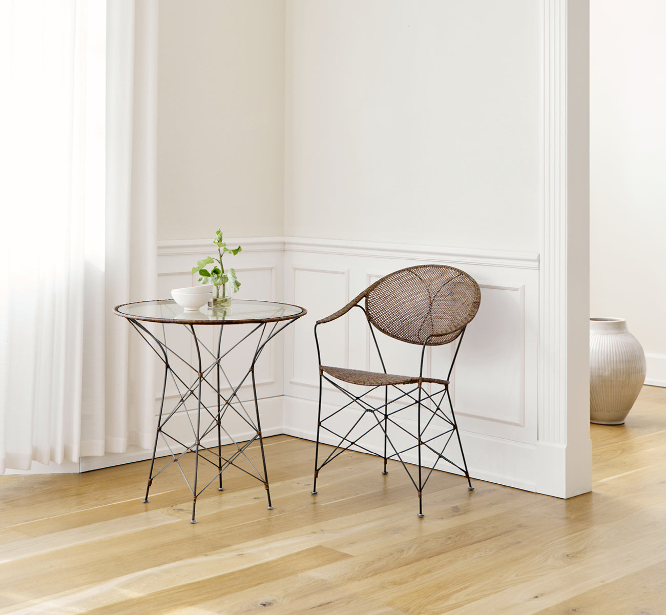 Dies ist ein Lifestyle-Bild von Funky Esszimmerstuhl in hazelnut rattan iron frame, in einem hellen Interieur mit weißen Wandpaneelen und.