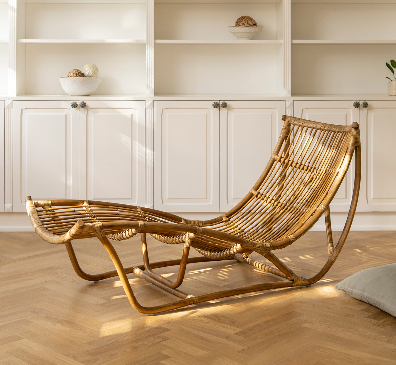 Dies ist ein Lifestyle-Bild von Michelangelo Daybed i antique rattan. Platziert in einem sonnendurchfluteten weißen Raum mit Fischgrätparkett.