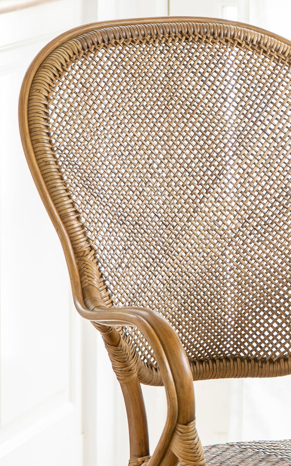 Dies ist ein Nahaufnahmebild von Rossini Esszimmer-Armlehnstuhl in antique rattan. Detail der gebogenen Rattan-Armlehne, des geflochtenen Sitzes und der umwickelten Verbindungen.