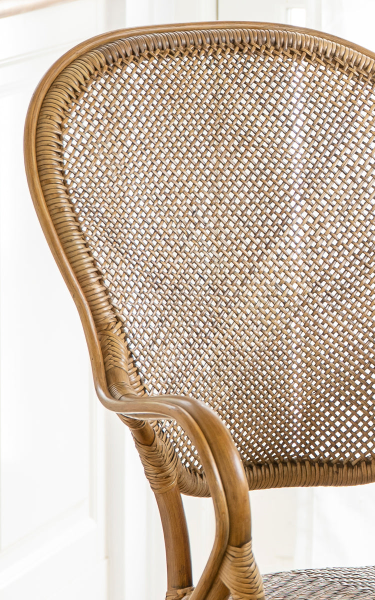 Dies ist ein Nahaufnahmebild von Rossini Esszimmer-Armlehnstuhl in antique rattan. Detail der gebogenen Rattan-Armlehne, des geflochtenen Sitzes und der umwickelten Verbindungen.