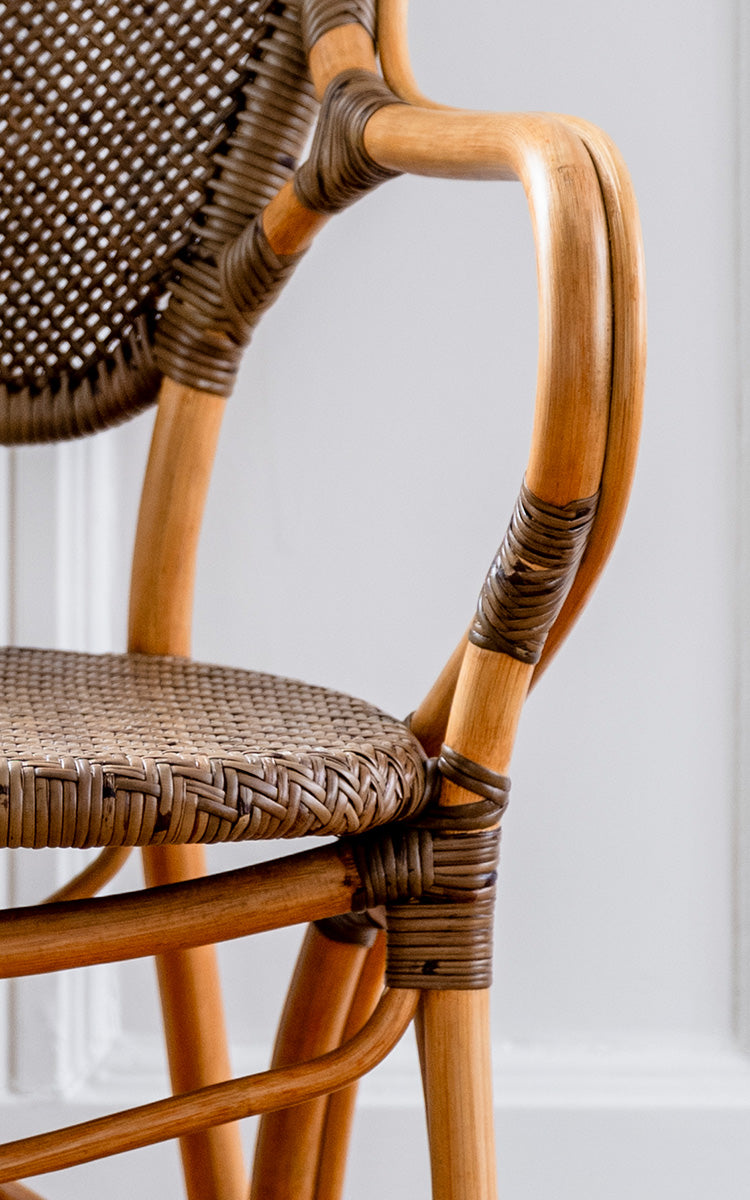 Dies ist ein Nahaufnahmebild von Rossini Armlehnstuhl in cherry rattan. Zweifarbige Kirsch-Korbrückenlehne mit naturfarbenem gebogenem Rahmen und geflochtenem Sitz.