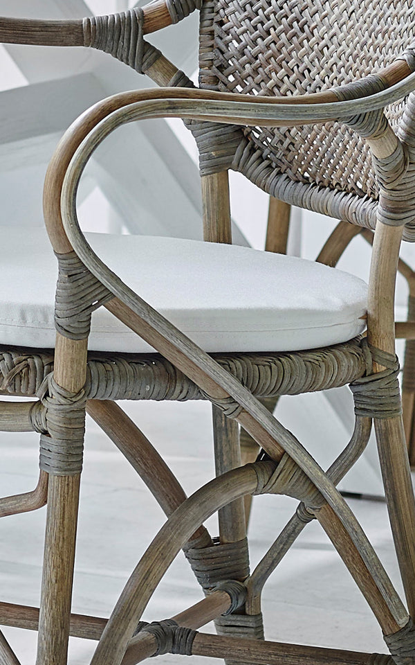 Dies ist ein Nahaufnahmebild von Rossini Armlehnstuhl in taupe rattan. Detail des verwitterten taupe-farbenen Rattans mit weißem Sitzkissen.