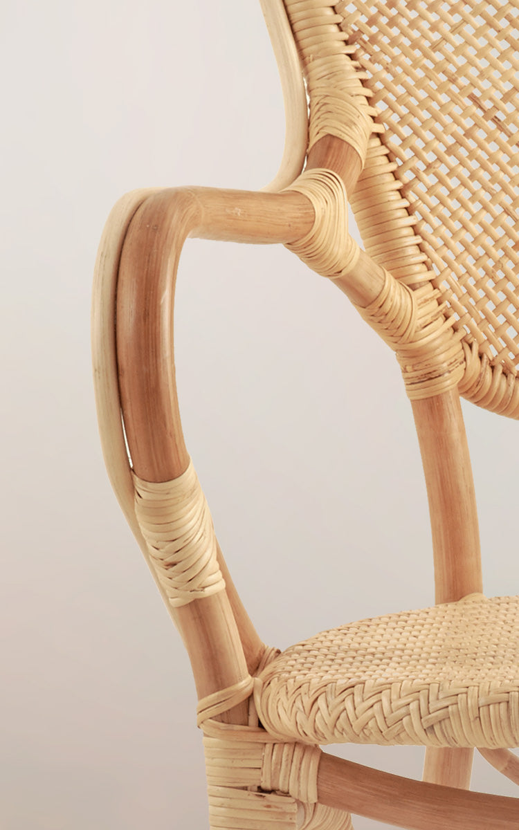 Dies ist ein Nahaufnahmebild von Rossini Esszimmer-Armlehnstuhl in natural rattan. Detail der hellen Rattan-Armlehnenkurve und des Fischgräten-Geflechtsitzes.
