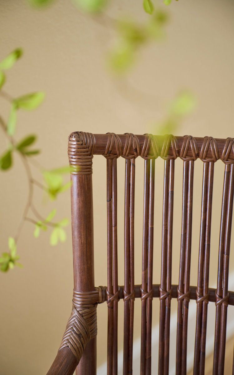 Dies ist ein Nahaufnahmebild von Piano Esszimmerstuhl in brown rattan. Umwickelte Rattansprossen der Lehne im weichen Licht.