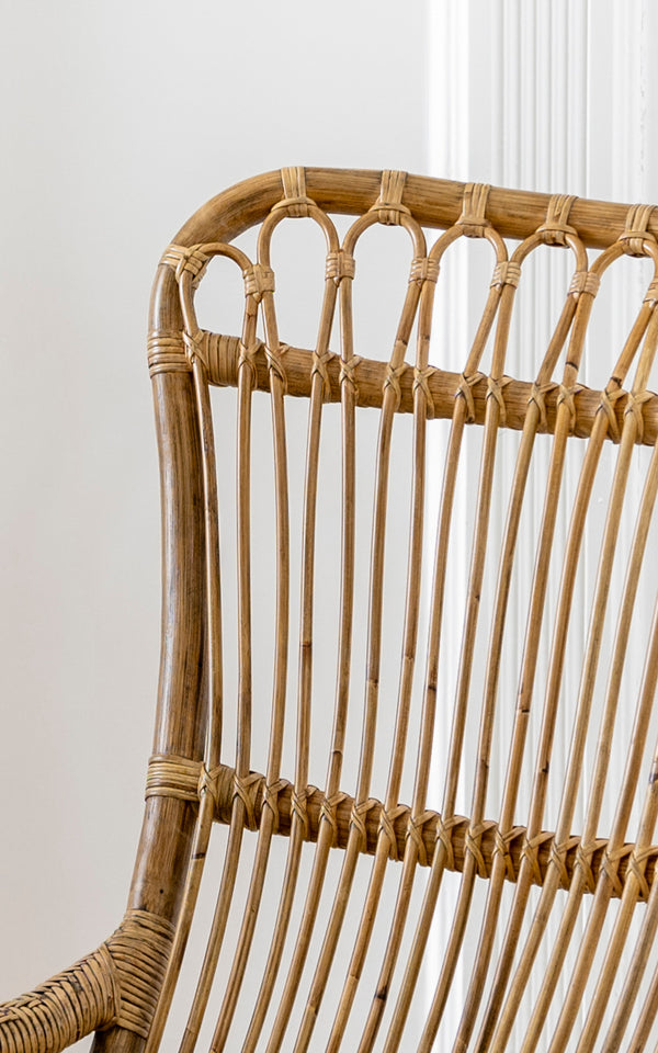 Dies ist ein Nahaufnahmebild von Monet Rocking Chair i antique rattan. Detail der Schlaufenbogen-Rückenlehne und der vertikalen Rattanstab-Konstruktion.