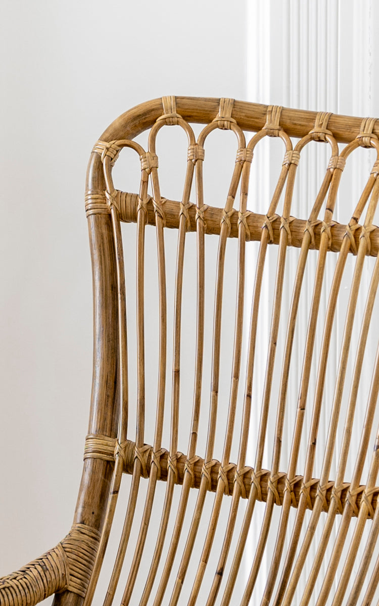 Dies ist ein Nahaufnahmebild von Monet Rocking Chair i antique rattan. Detail der Schlaufenbogen-Rückenlehne und der vertikalen Rattanstab-Konstruktion.