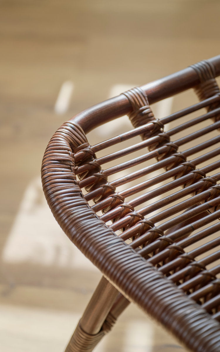 Dies ist ein Nahaufnahmebild von Monet Fußhocker in brown rattan. Geschwungener Rattanrahmen mit umwickelten Streben.