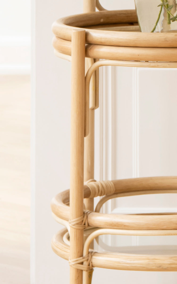 Dies ist ein Nahaufnahmebild von Romeo Trolley i natural rattan. Detail des zweistöckigen Rattangestells mit Glasablage und Messingrädern.
