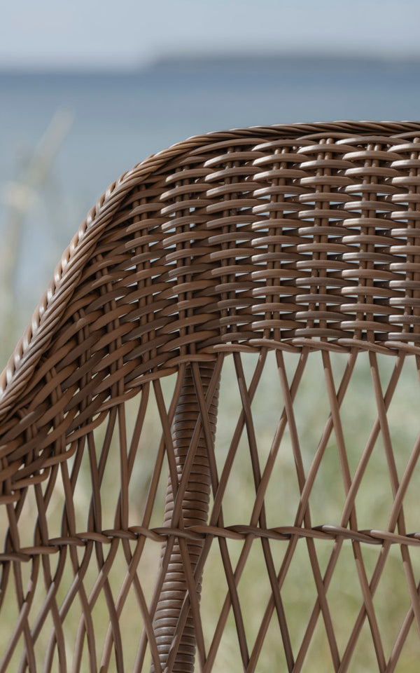 Dies ist ein Nahaufnahmebild von Charlot 3-Sitzer-Außensofa in brown artfibre aluminum. Offen geflochtene Rückenlehne vor Meerblick.
