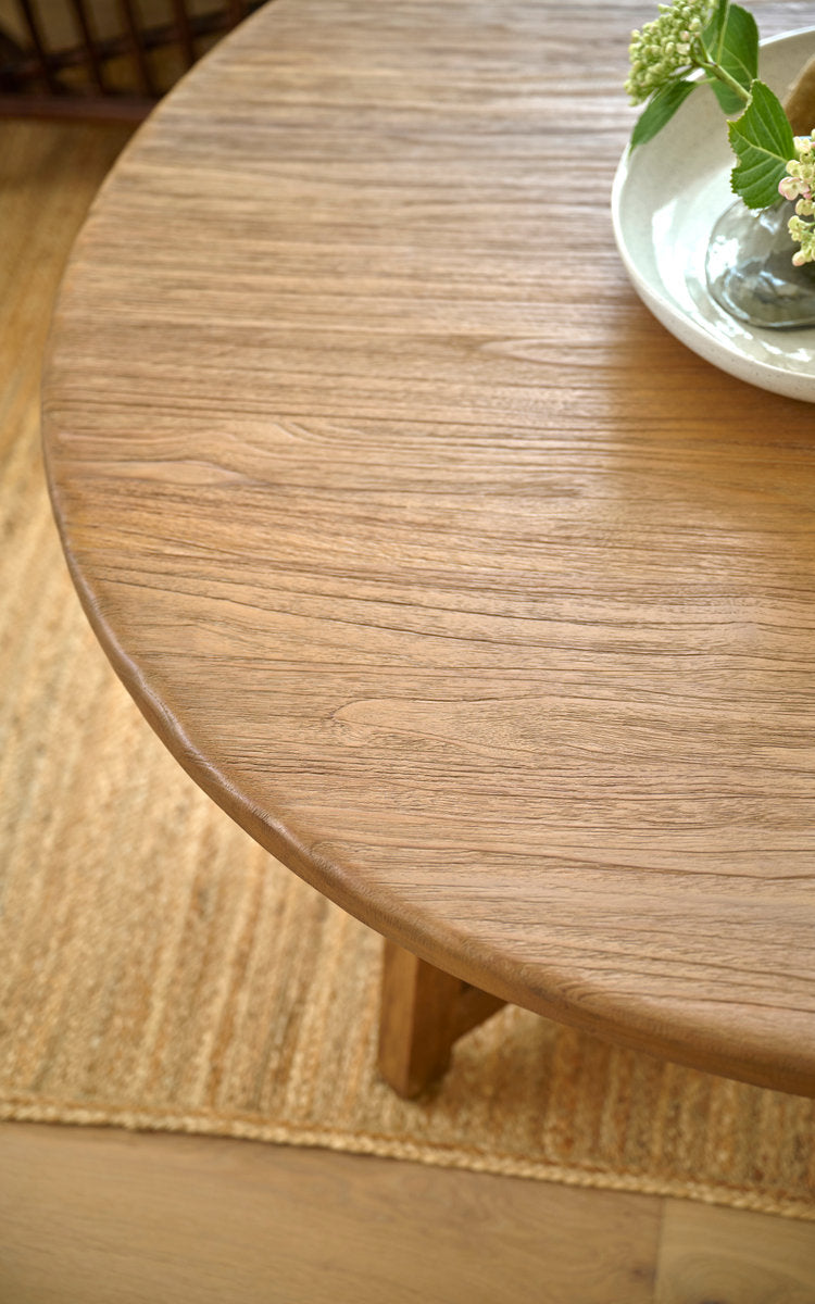Dies ist ein Nahaufnahmebild von Aksel Couchtisch Ø120 cm in teak indoor. Runde Teakplatte mit Blumen in einer Schale auf Juteteppich.