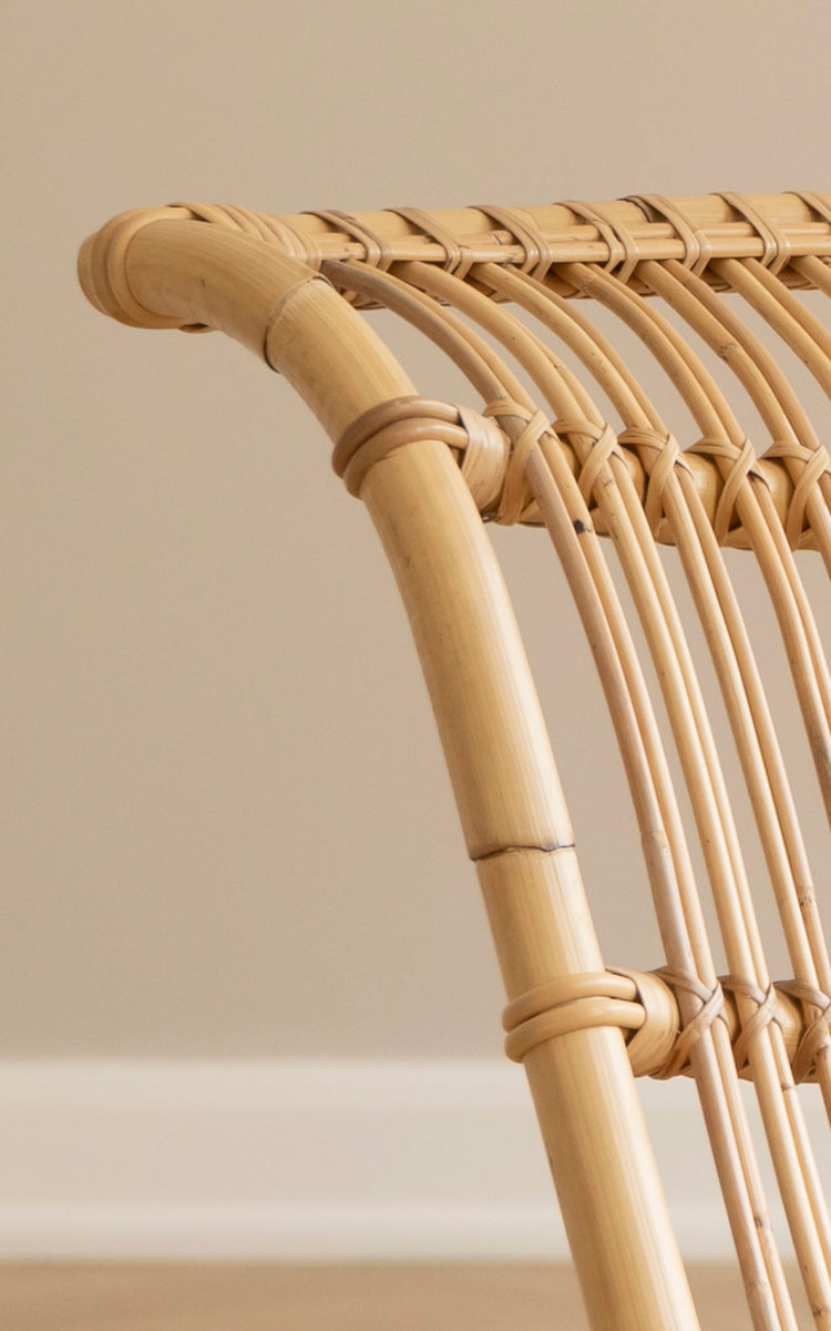 Dies ist ein Nahaufnahmebild von Paris Lounge-Sessel in polished natural rattan. Detail des geschwungenen Rattanrahmens und der bogenförmigen Sitzlatten.