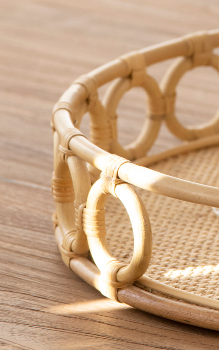 Dies ist ein Nahaufnahmebild von Mira Tray i natural rattan. Detail des kreisförmigen Ringrandes und des geflochtenen Rohrbasis des runden Tabletts.