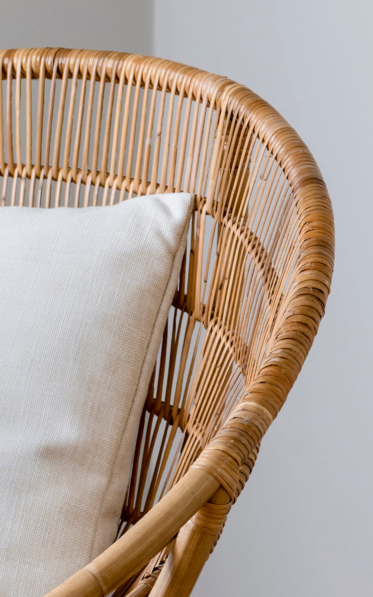 Dies ist ein Nahaufnahmebild von Luna Lounge-Sessel in natural skin on rattan. Der geschwungene Rahmen mit vertikalen Lamellen und weißem Kissen betonen das Design.