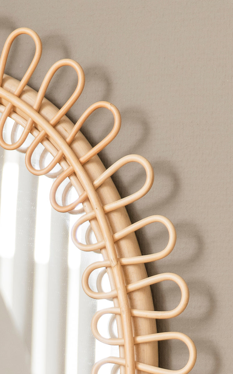 Dies ist ein Nahaufnahmebild von Luella Spiegel in polished natural rattan. Der dekorative geschlungene Rattanrahmen wirft elegante Schatten an die Wand.