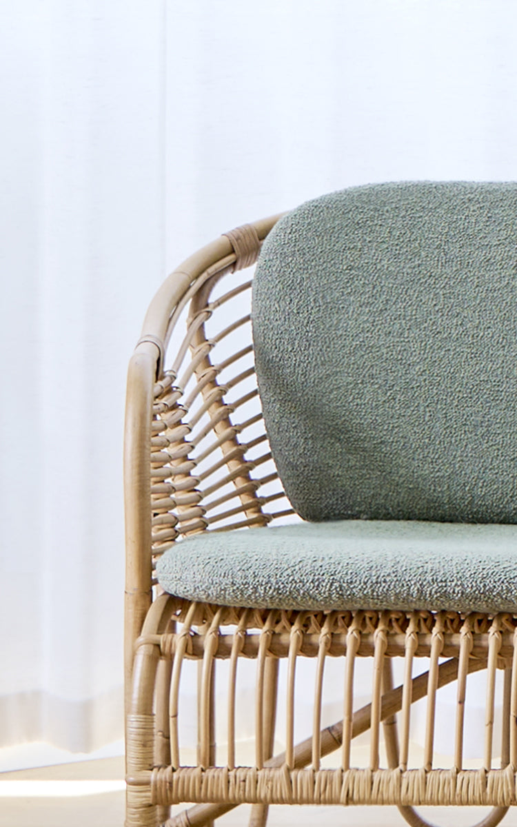 Dies ist ein Nahaufnahmebild von Swing Sofa in polished natural rattan. Detail des gebogenen Rattan-Sofarahmens mit Bouclé-Sitzkissen.