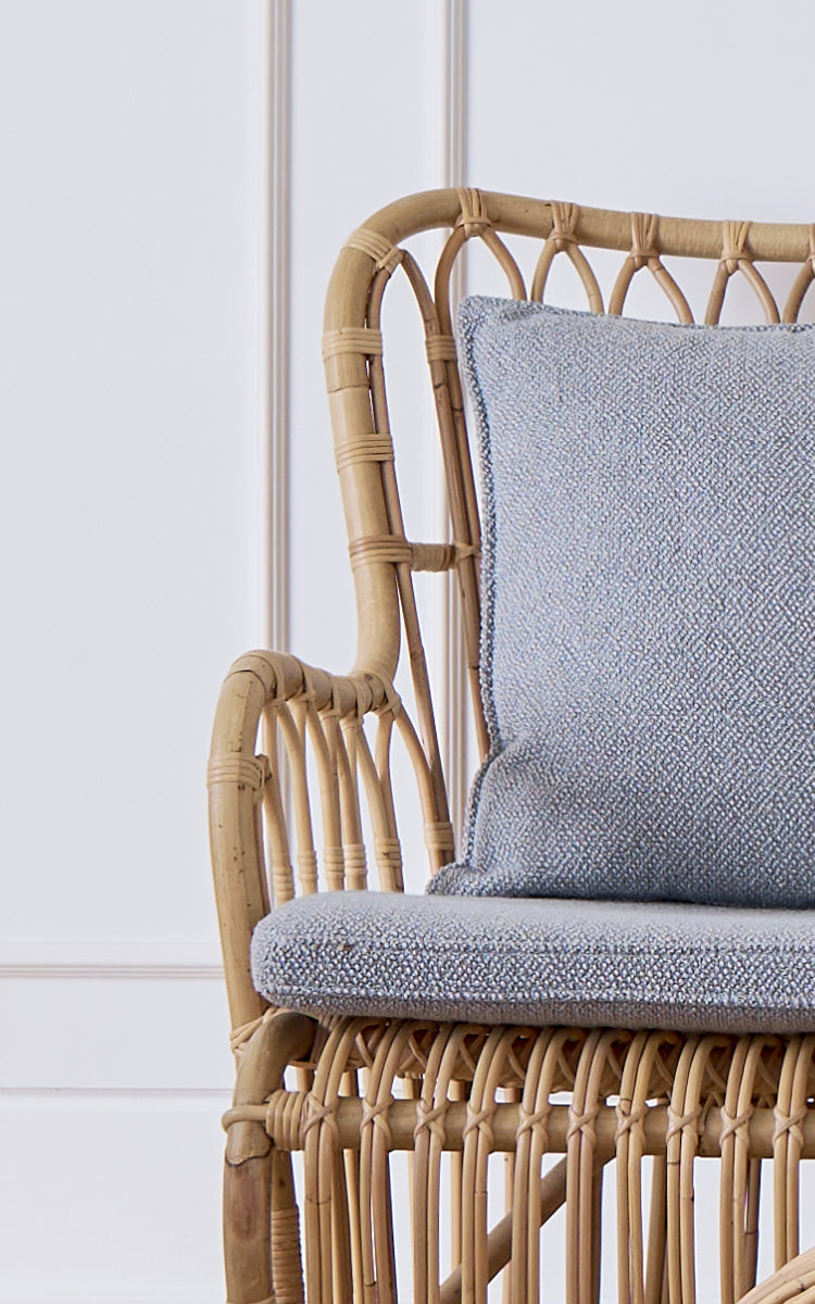 Dies ist ein Nahaufnahmebild von Tulip Sofa in polished natural rattan. Detail des Rattan-Sofarahmens mit gebogenen Streben und Bouclé-Kissen.