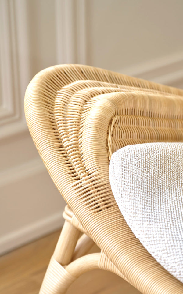 Dies ist ein Nahaufnahmebild von Pacifique Lounge-Sessel in natural core weave rattan frame. Geflochtene Schale mit weißem Kissen vor vertäfelter Wand.