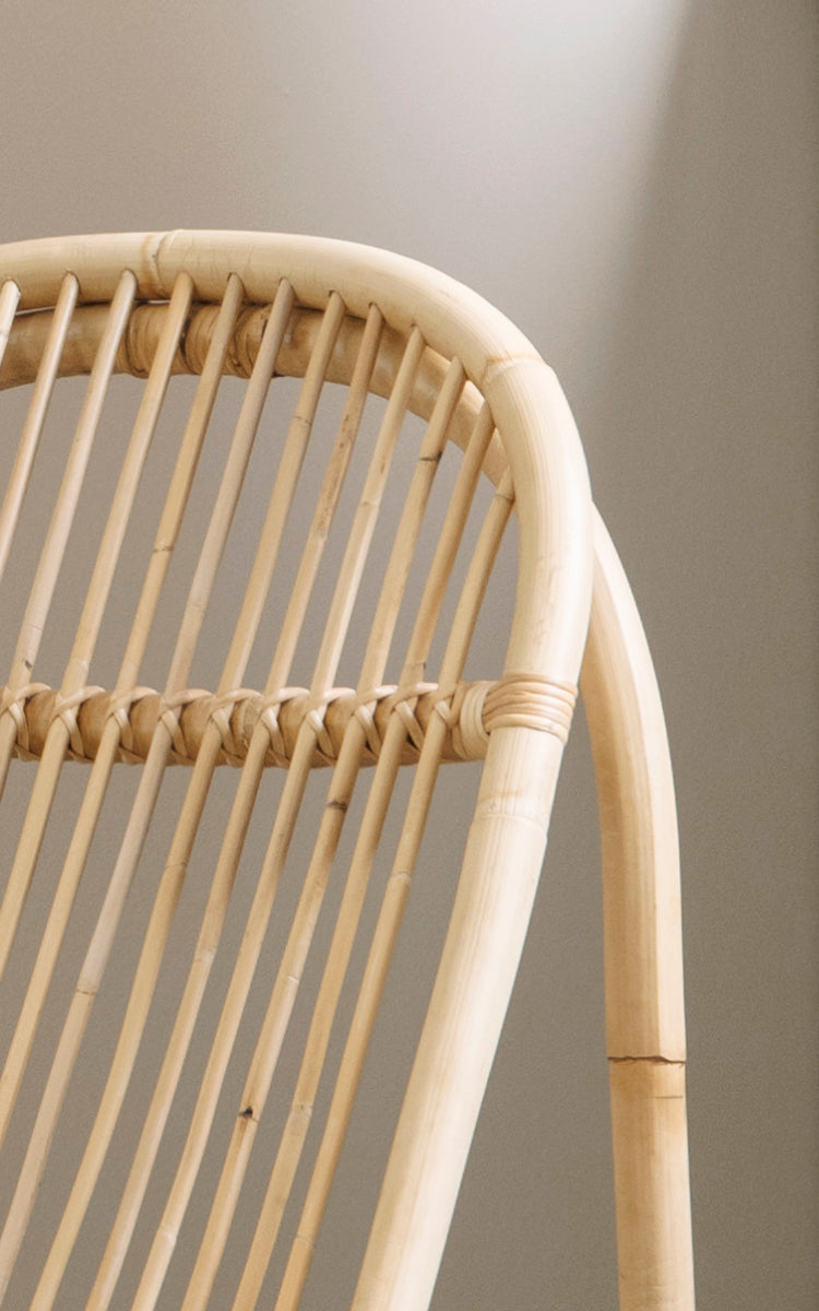 Dies ist ein Nahaufnahmebild von Nanny Rocking Chair i polished natural rattan. Detail der glatten gebogenen Stäbe und der kreisförmigen Kufenbasis.