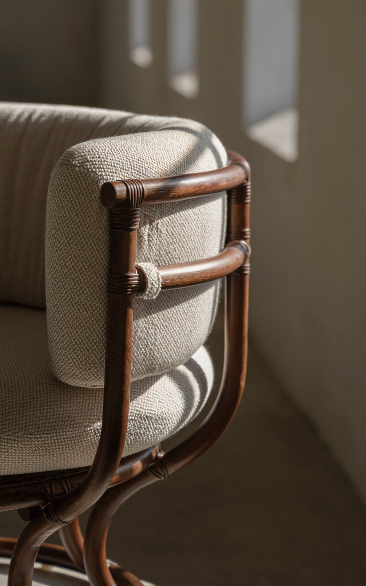 Dies ist ein Nahaufnahmebild von Coco Lounge-Sessel in brown rattan. Umwickelte Armlehne und weiches Kissen im Tageslicht.