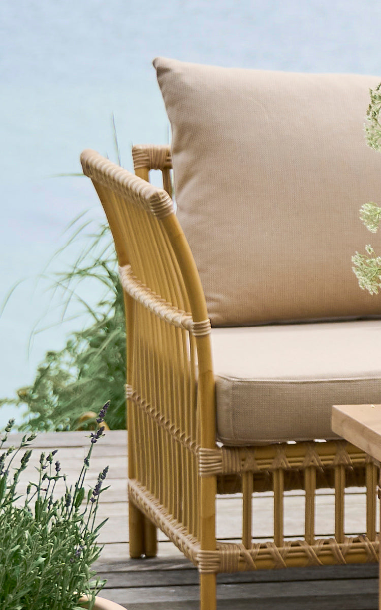 Dies ist ein Nahaufnahmebild von Maggie Sofa Eckmodul in natural aluminium artfibre. Vertikaler Lattenrahmen mit umwickelten Verbindungen und beigem Kissen.