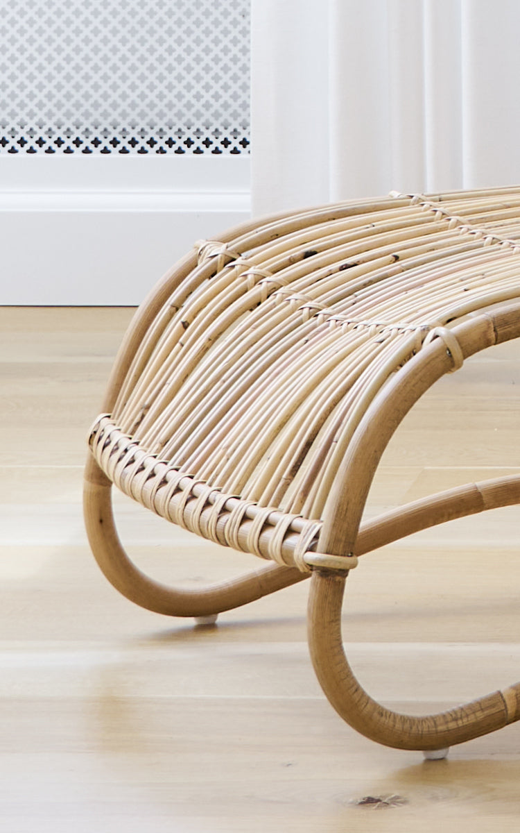 Dies ist ein Nahaufnahmebild von Teddy Fußhocker in polished natural rattan. Detail der gebogenen Rattanleisten und der geflochtenen Umwicklung des Fußhockers.